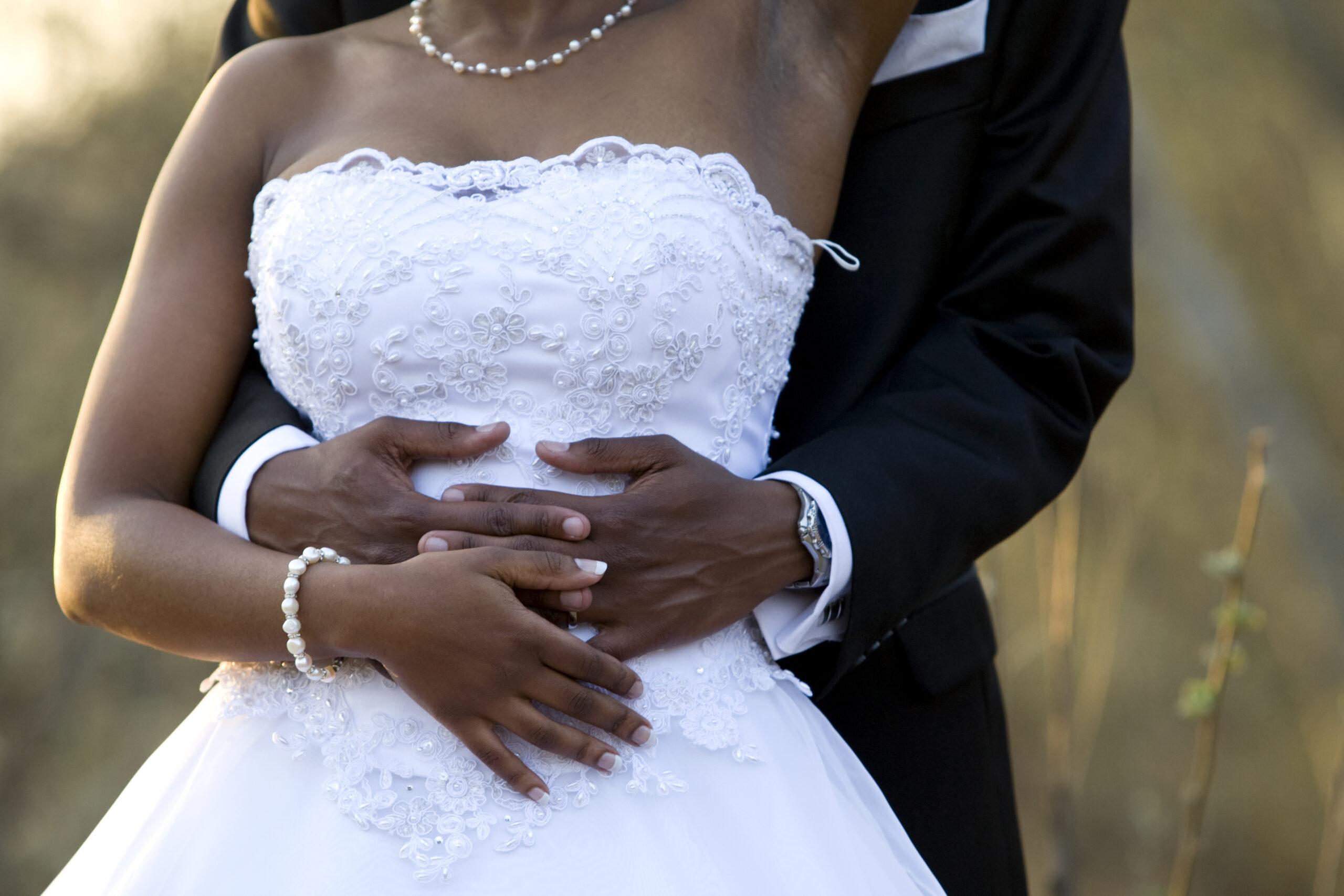 Black newlyweds, man standing behind the woman with their hands clasped around her